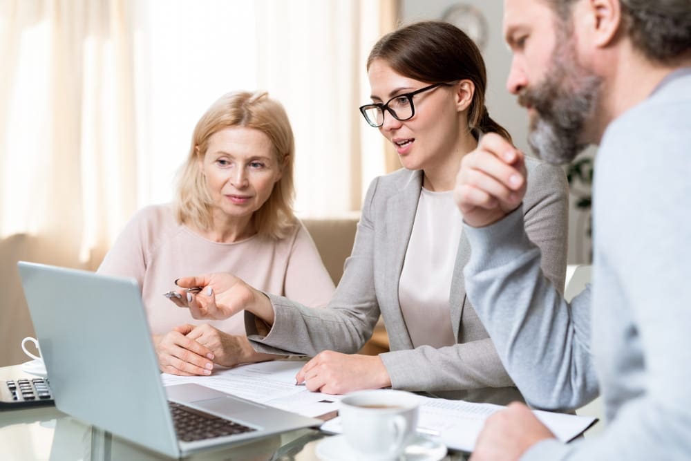 Financial adviser discussing cohabitation and nuptial agreements with parents and adult child, reviewing documents on a laptop to protect family contributions to property.